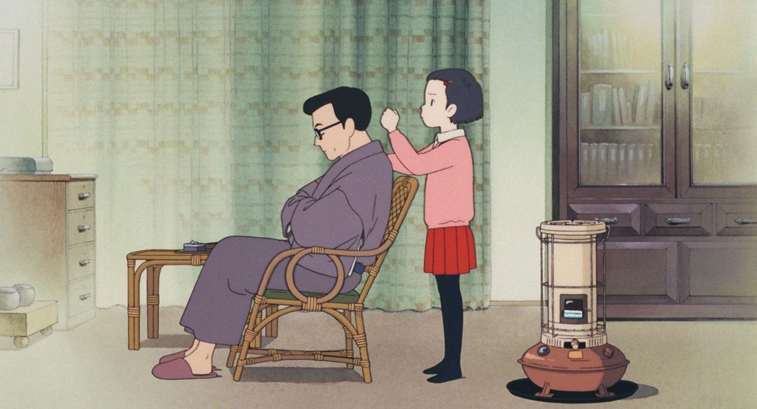 El padre, con gafas, sentado en la butaca de mimbre mientras Taeko le habla