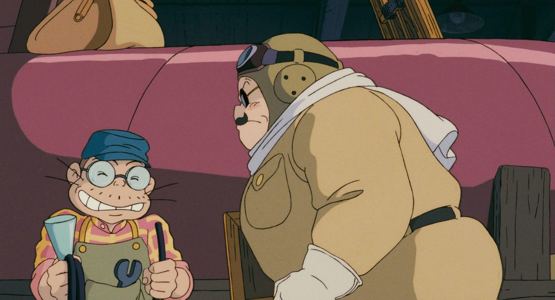 Piccolo, con gorra y gafas redondas, sentado delante de Porco