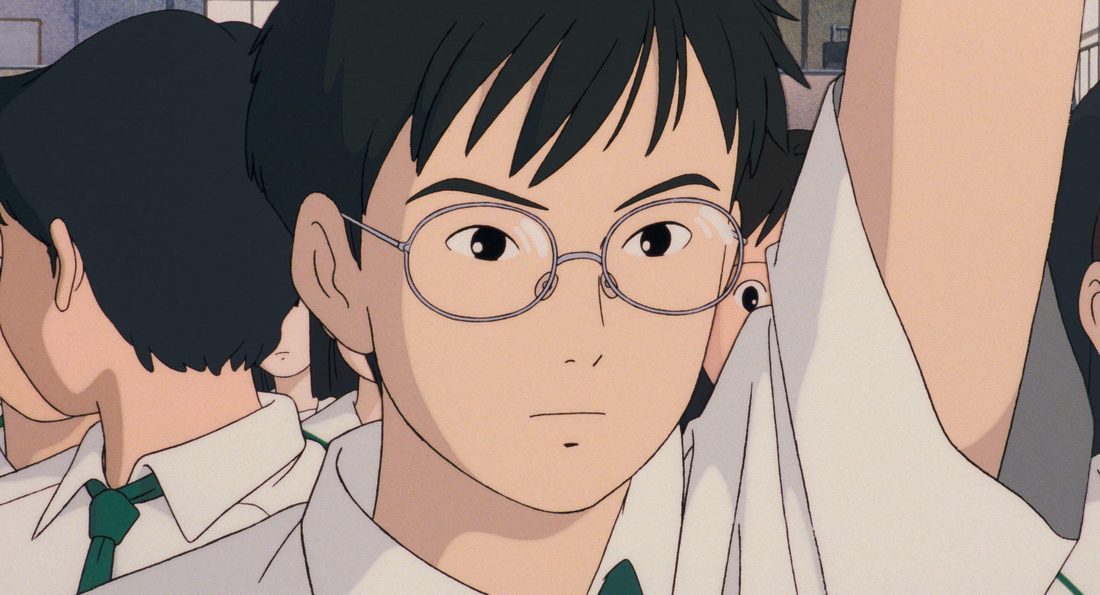Yutaka, con sus gafas y el uniforme, sentado en clase